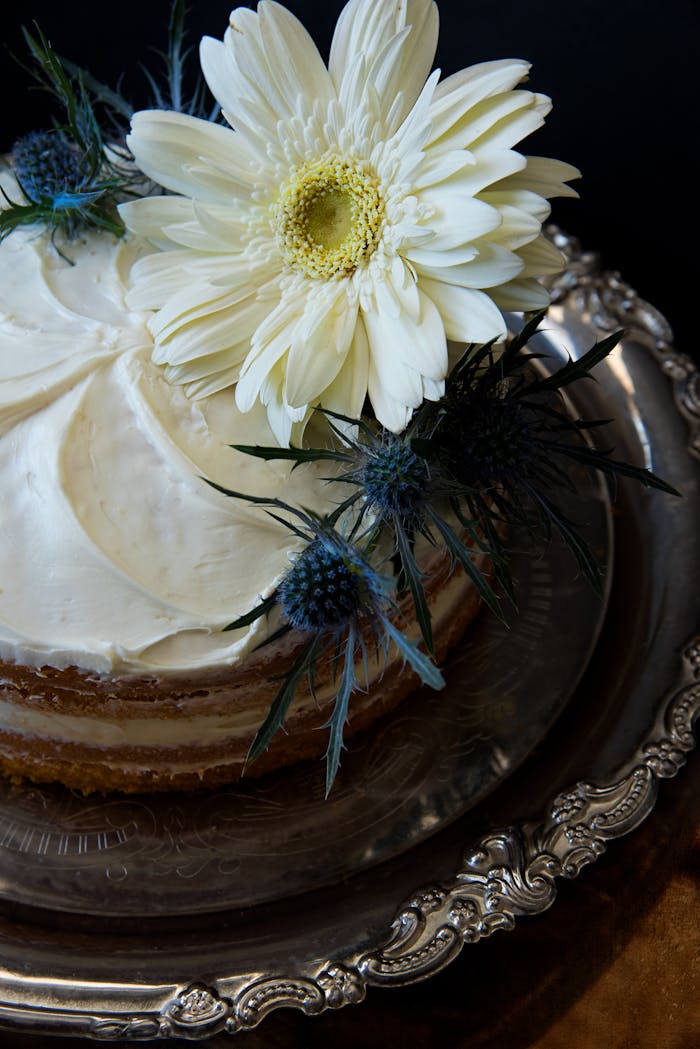 A beautifully decorated cake with white and blue flowers on an ornate silver tray.